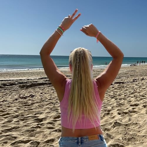 Person with long hair raising arms on a sandy beach