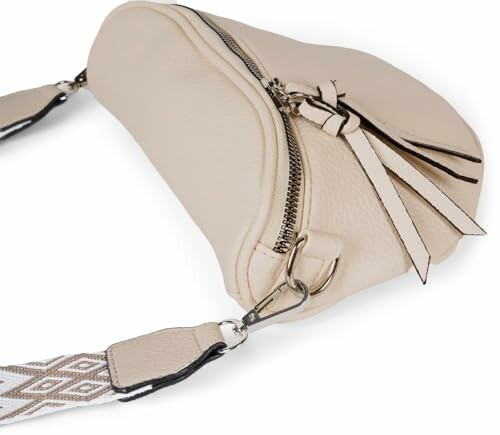 Beige leather crossbody bag with decorative strap and zipper.