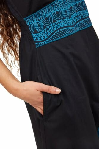Close-up of a black jumpsuit with blue patterns and a hand in the pocket.