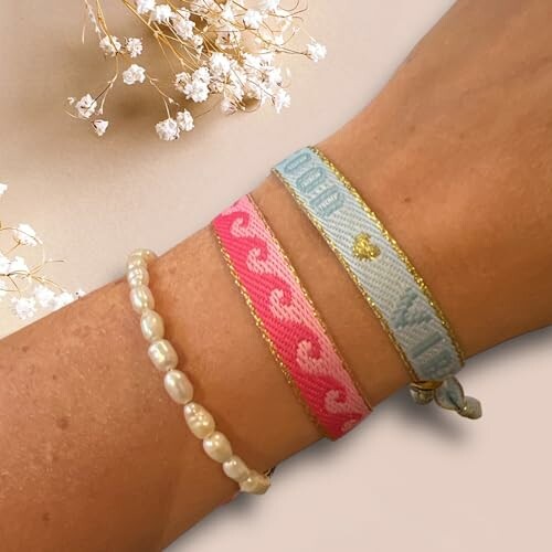 Three bracelets on an arm, including a pearl bracelet and two colorful woven bands.