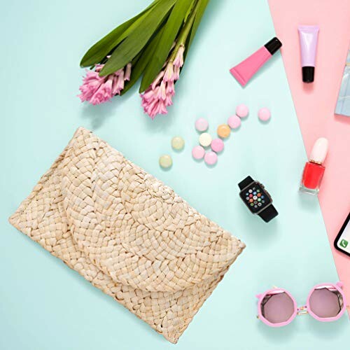Flat lay of fashion accessories including a woven clutch, sunglasses, flowers, makeup, and a watch.
