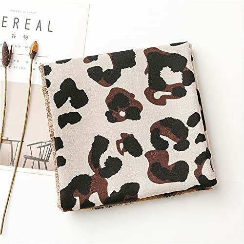 Folded leopard print fabric on a surface with dried flowers and a magazine.