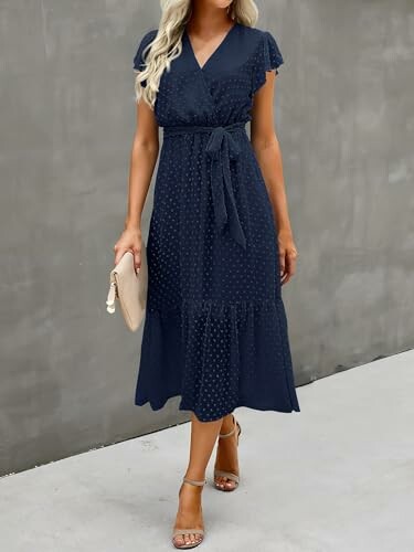 Woman in navy blue midi dress with belt, holding a clutch.