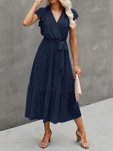 Woman wearing a navy blue wrap dress with a belt and holding a beige clutch.